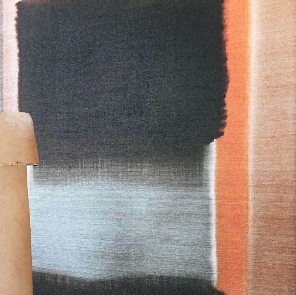 Abstracte Elitis Ceres wandbekleding in grijstinten met oranje accenten en een aardewerk lamp op de voorgrond.