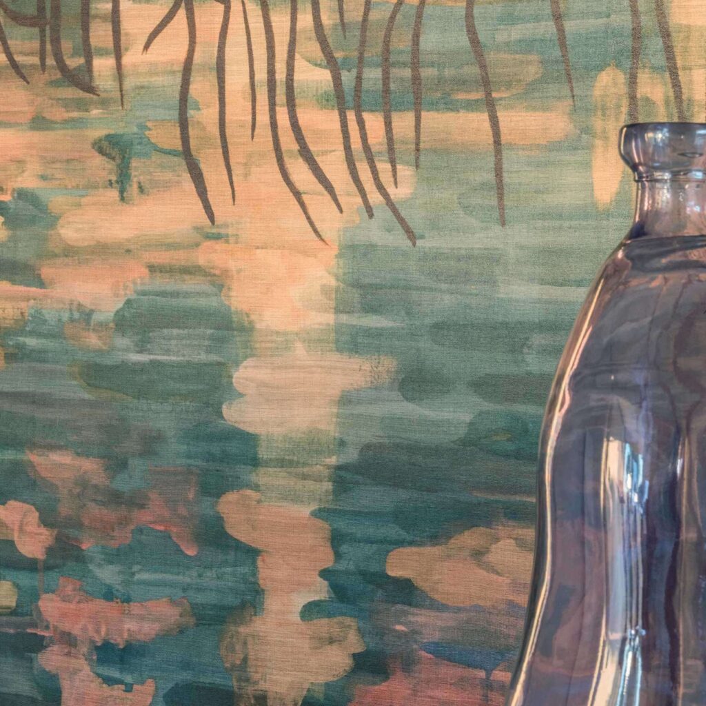 Detail van het Elitis Ceres Broceliande VP 1011-01 behang met een abstract geschilderd patroon in groen- en perziktinten, en een glazen vaas op de voorgrond.