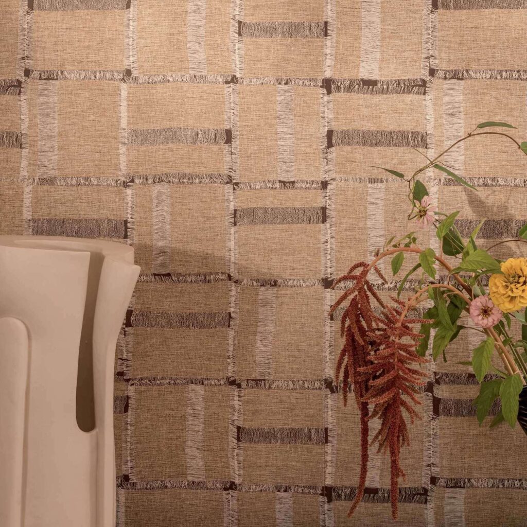 Beige Elitis Ceres Cybele VP 1009-02 behang met geweven structuur en subtiele franjes, gecombineerd met een vaas en bloemen.