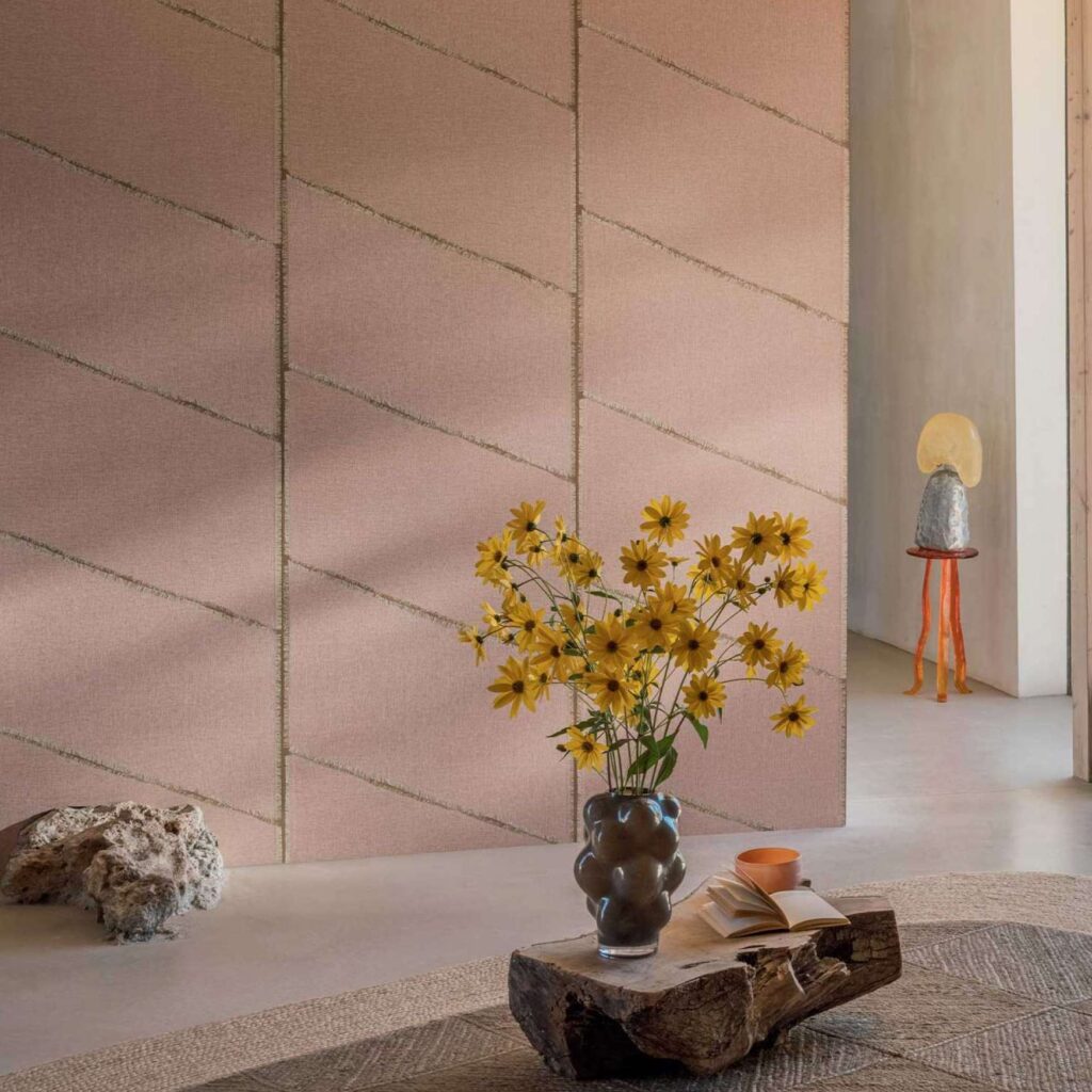 Moderne interieursetting met Elitis Ceres Hera VP 1010 03 wandbekleding in roze tint, een vaas met gele bloemen en een decoratief bijzettafeltje op de achtergrond.