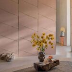 Moderne interieursetting met Elitis Ceres Hera VP 1010 03 wandbekleding in roze tint, een vaas met gele bloemen en een decoratief bijzettafeltje op de achtergrond.