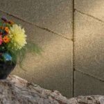 Detailopname van de Elitis Ceres Hera VP 1010 wandbekleding met zichtbare textuur, naast een vaas met kleurrijke bloemen op een rotsachtig oppervlak.
