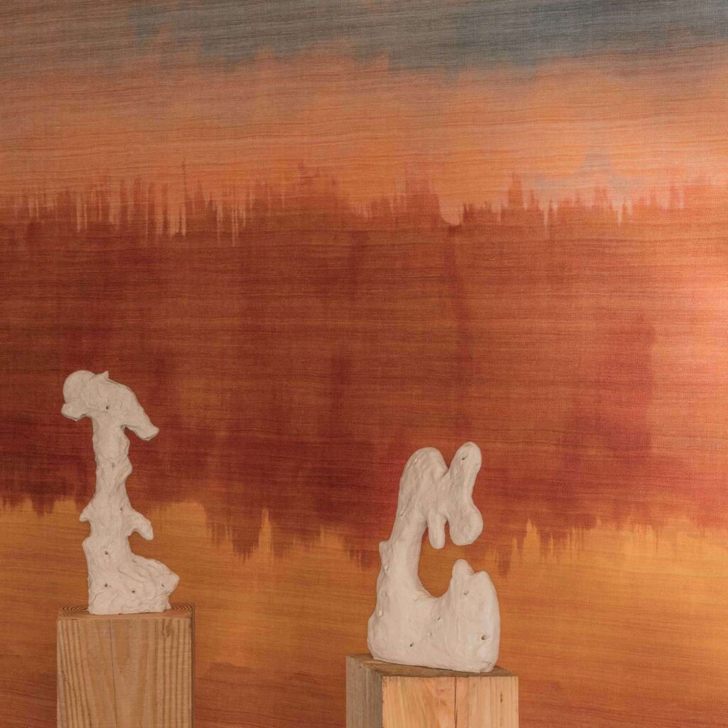 Twee abstracte, witte sculpturen op houten sokkels voor een Elitis Ceres Proserpine VP 1012-01 wandbekleding met warme oranje en roodbruine tinten.