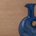 Blauwglazen vaas met ronde uitsparing voor een beige Elitis Ceres Rhea VP 1008 textuurbehang.