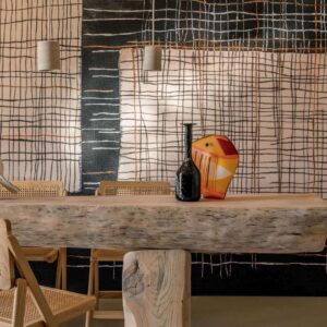 Houten eettafel met rotan stoelen en decoratieve vazen, voor een wand met Elitis Ceres Sashiko VP 1013-01 behang in abstract ruitpatroon.