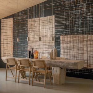 Sfeervolle eetkamer met een lange houten tafel, rotan stoelen en een Elitis Ceres Sashiko VP 1013-01 wandbekleding met grafisch patroon.