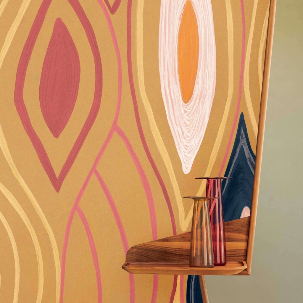Gekleurde muur met abstract patroon uit de Elitis Cordes Sensibles x Véronique de Soultrait collectie, met een houten plankje en twee glazen vazen.