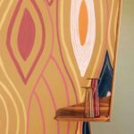 Gekleurde muur met abstract patroon uit de Elitis Cordes Sensibles x Véronique de Soultrait collectie, met een houten plankje en twee glazen vazen.