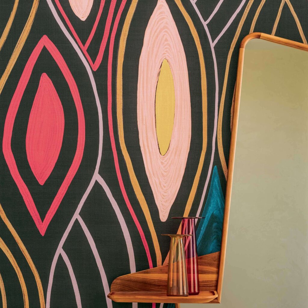 Detail van het Elitis Cordes Sensibles x Véronique de Soultrait Arabesque VP 1002-02 behang met kleurrijk abstract patroon, naast een houten plank met glazen vazen en een spiegel.