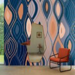 Interieur met kleurrijk Elitis Cordes Sensibles Arabesque behang, een geometrische spiegel en een oranje fauteuil.