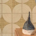 Decoratieve wandbekleding uit de Elitis Cordes Sensibles collectie met geometrisch patroon en een sculptuur op een houten oppervlak op de voorgrond.