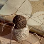 Twee rollen touw liggen op een kunstzinnig Elitis Cordes Sensibles x Véronique de Soultrait wandpaneel met gebogen lijnen en natuurlijke texturen.