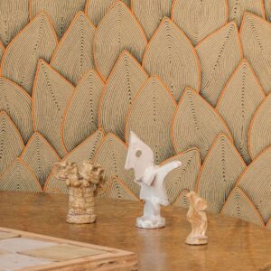 Gedetailleerd Elitis Cordes Sensibles behang in bladmotief met oranje accenten, met keramische sculpturen op een houten tafel.