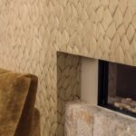 Detail van een modern interieur met Elitis Cordes Sensibles behang van Véronique de Soultrait in het patroon Jonchée, rondom een haard met natuurstenen onderkant.