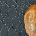 Detail van het Elitis Cordes Sensibles behang met bladpatroon in reliëf en een transparant amberkleurig object op de voorgrond.