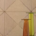 Textuurwand Elitis Cordes Sensibles met geometrisch patroon en twee glazen vazen in amber en groen.
