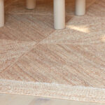 Beige Elitis Coyoacan vloerkleed met subtiele textuur onder een lichtgekleurde tafel.