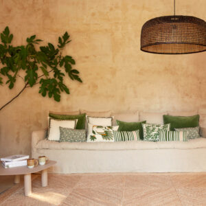 Sfeervolle zithoek met het Elitis Coyoacan vloerkleed, een neutrale bank met groene kussens en een natuurlijke wandlamp.