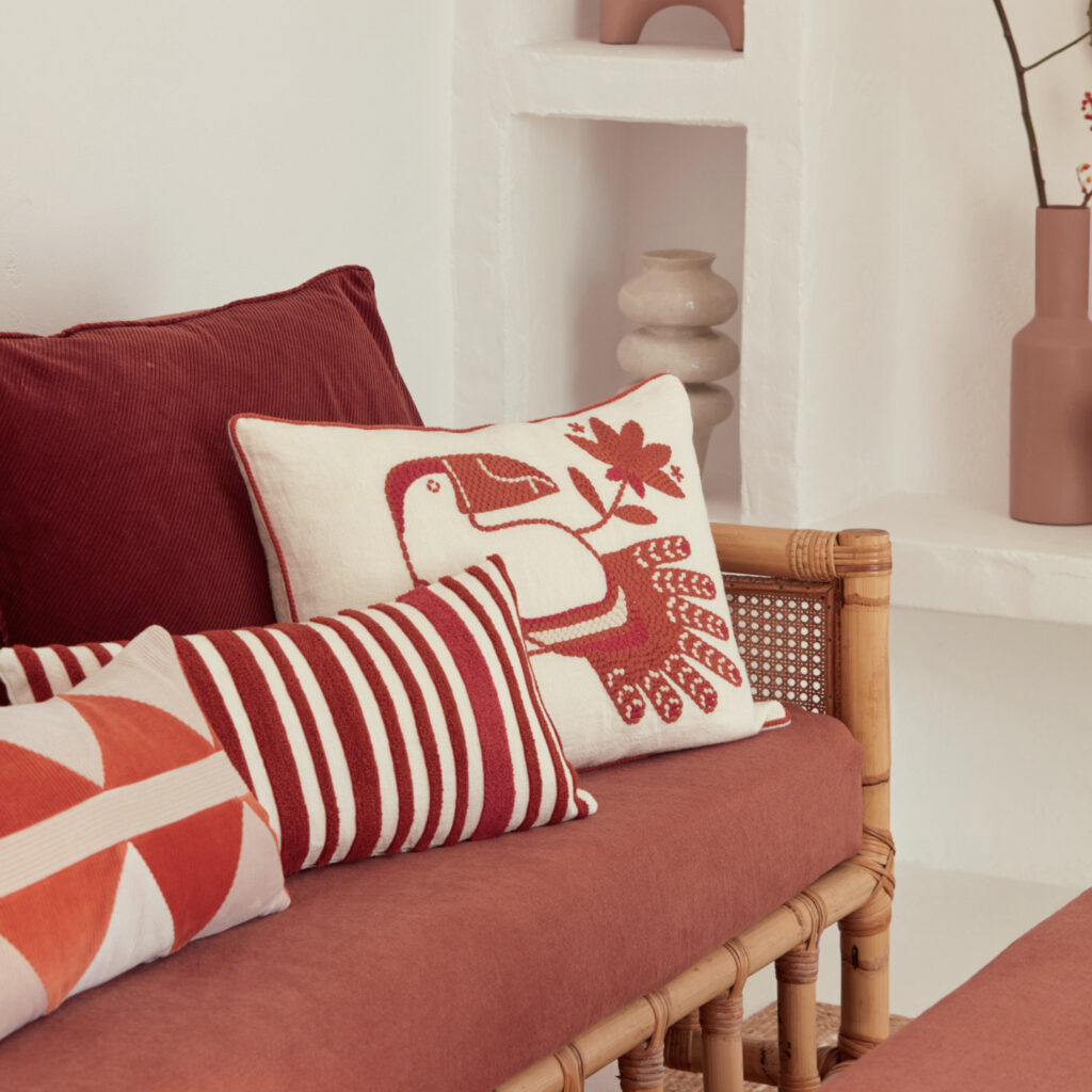 Rood Elitis Cristobal kussen met vogelmotief op een rotan bank in een sfeervolle minimalistische woonkamer.