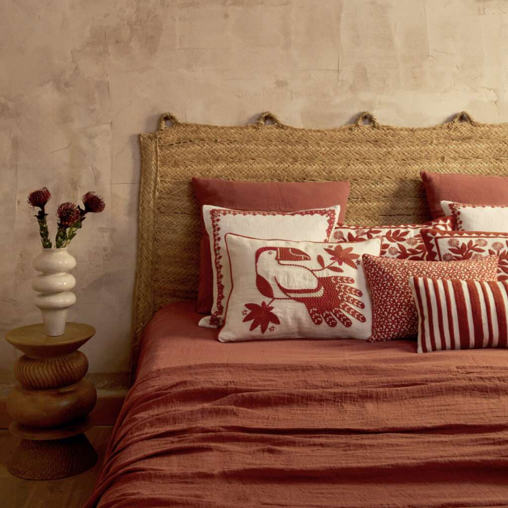 Sfeervolle slaapkamer met Elitis Cristobal kussen in rood-wit ontwerp met tropische print op een bed met rood textiel en rotan hoofdbord.