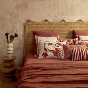 Sfeervolle slaapkamer met Elitis Cristobal kussen in rood-wit ontwerp met tropische print op een bed met rood textiel en rotan hoofdbord.