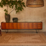 Interieur in warme aardetinten met het Elitis Diego et Frida TA 128 05 04 vloerkleed voor een houten dressoir en grote plant.