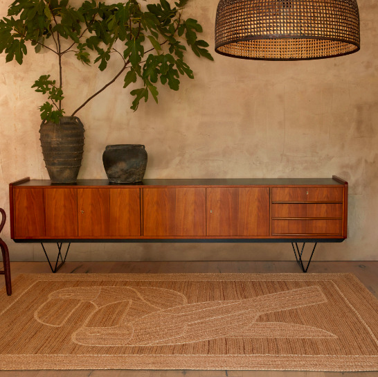Interieur in warme aardetinten met het Elitis Diego et Frida TA 128 05 04 vloerkleed voor een houten dressoir en grote plant.