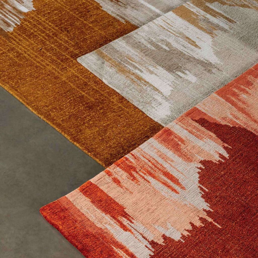 Detail van het Elitis Emile TA 135 17 02 vloerkleed met abstract patroon in warme aardetinten zoals rood, oranje en beige.