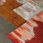 Detail van het Elitis Emile TA 135 17 02 vloerkleed met abstract patroon in warme aardetinten zoals rood, oranje en beige.