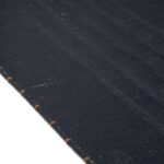 Detailopname van het Elitis Ernest TA 132 81 02 vloerkleed met een donker geweven structuur en lichte stiksels langs de rand.