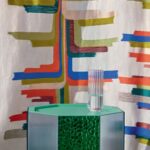 Glazen vaas op een groene designkast met daarachter Elitis Excentric Boty stof met kleurrijk grafisch patroon.