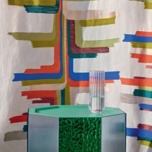 Glazen vaas op een groene designkast met daarachter Elitis Excentric Boty stof met kleurrijk grafisch patroon.
