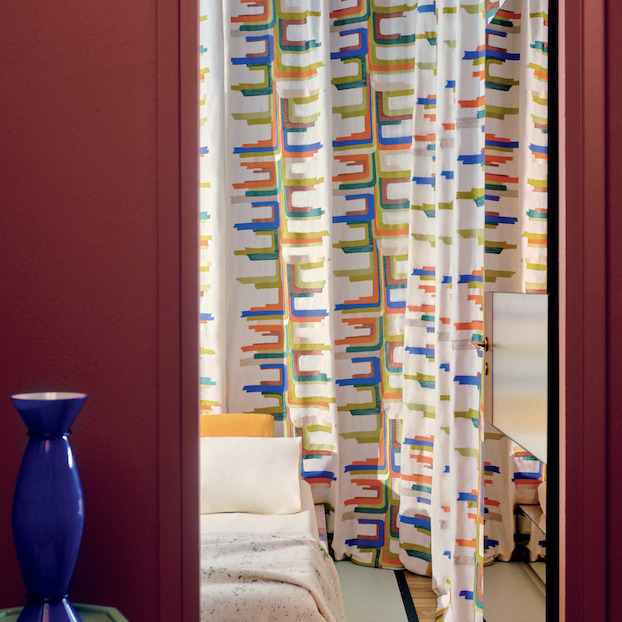 Slaapkamer met kleurrijk geometrisch Elitis Excentric Boty gordijn achter een open deuropening.