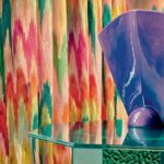 Kleurrijke Elitis Excentric Groovy gordijnstof met een abstract patroon achter een glazen tafel met een glanzend paarse vaas.