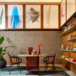 Moderne zithoek met Elitis Forms Twisted Suedine behang, een ronde tafel, designstoelen en kleurrijke kunst aan de muur.