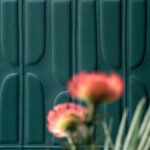 Detailopname van Elitis Forms Twisted Suedine behang in donkergroen met een onscherpe bloem op de voorgrond.