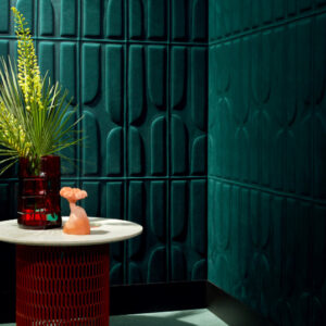 Moderne interieurhoek met Elitis Forms Twisted Suedine behang in donkergroen, een ronde tafel met decoratief rood onderstel en opvallende accessoires.