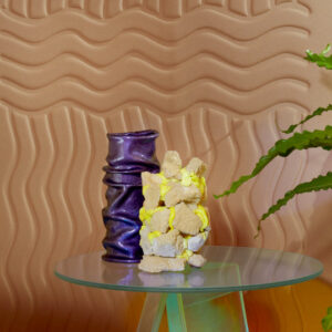 Designvaas en kunstobject op glazen tafel met golvend Elitis Forms Wall Wave Flanelle RM 1055 05 behang op de achtergrond.