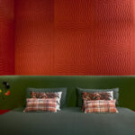 Slaapkamer met Elitis Forms Wall Wave Flanelle wandbekleding in roodtinten en een donkergroen bed met decoratieve kussens.