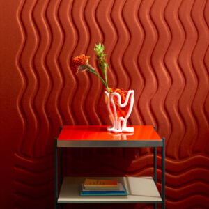 Een modern tafeltje met een golvende vaas en bloemen staat voor een rode Elitis Forms Wall Wave Flanelle wand met reliëf.