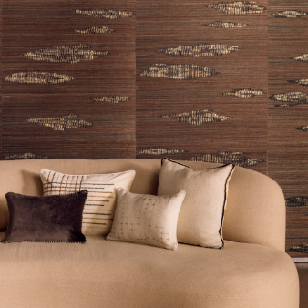 Beige bank met vier Elitis sierkussens voor een wand met een bruin, textuurachtig patroon.