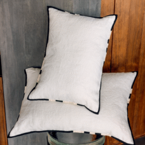 Twee Elitis Hudson sierkussens in wit met zwarte bies, gestyled tegen een houten en betonnen achtergrond.