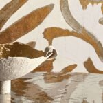 Detail van Elitis Kintsugi Algues Dorées behang met goudkleurige abstracte vormen en een ruwe keramieken schaal op een reflecterend oppervlak.