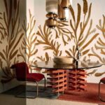 Sfeervolle interieursetting met Elitis Kintsugi Algues Dorées behang, ronde tafel met artistiek onderstel en moderne verlichting.
