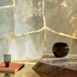 Sfeervolle interieursetting met Elitis Kintsugi Eclat VP 1022-01 behang, een glazen vaas en een donker drinkglas op een marmeren tafel.