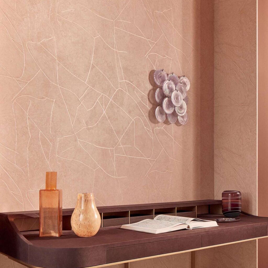 Interieur met Elitis Kintsugi behang in zachte roze tinten, een kunstige wanddecoratie en een stijlvol bureau met decoratieve voorwerpen.