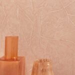 Beige Elitis Kintsugi wandbekleding met subtiel reliëf en oranjetinten decoratieve vazen op de voorgrond.