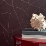 Donkerbruine Elitis Kintsugi-muur met metallic breuklijnen, naast een rode tafel met boeken en een decoratieve schaal.