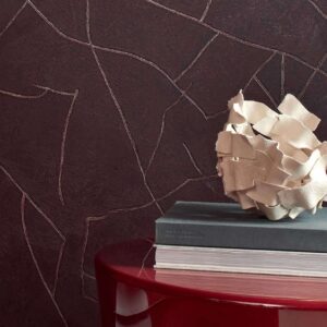 Donkerbruine Elitis Kintsugi-muur met metallic breuklijnen, naast een rode tafel met boeken en een decoratieve schaal.
