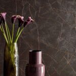 Twee designvazen met bloemen staan voor een donkere Elitis Kintsugi muur met goudkleurige scheurpatronen.